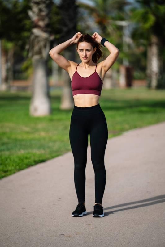 Young female runner getting ready to run morning cardio exercise. Woman athlete tying her hair in a ponytail before training and workout.