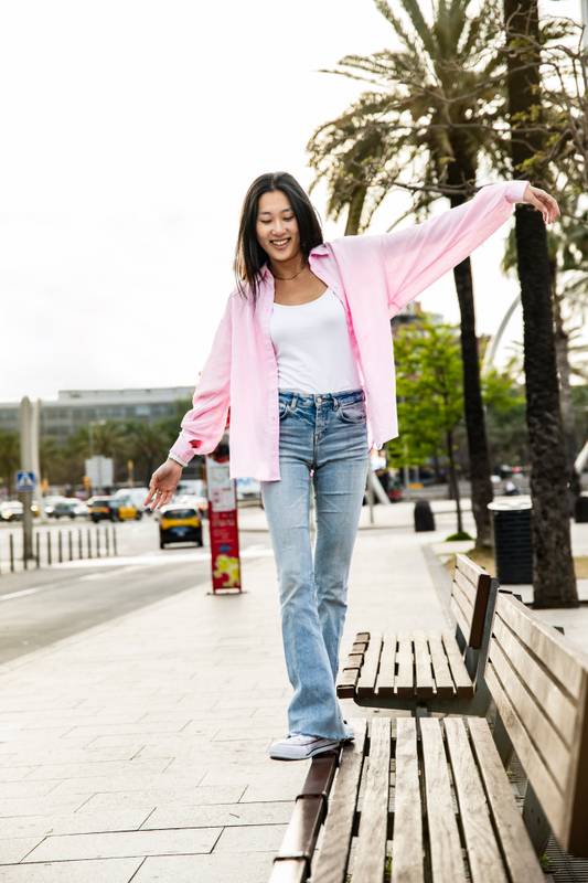 Young smiling woman balancing on bench in the street. Carefree and relaxed lady walking on bench park with her arms outstretched in a city.