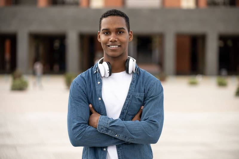 Young handsome guy smiling and looking at camera relaxed.Satisfied man smiling and standing with arms crossed wearing headphones.