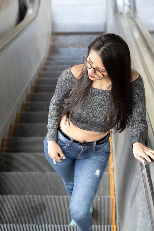 from a top perspective, a beautiful young latin woman standing up on an escalator, lifestyle