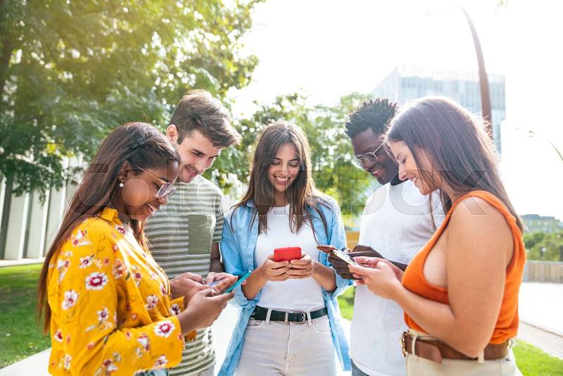 happy young friends looking mobile phone and smiling - five happy teenagers with a smartphone - Lifestyle concept