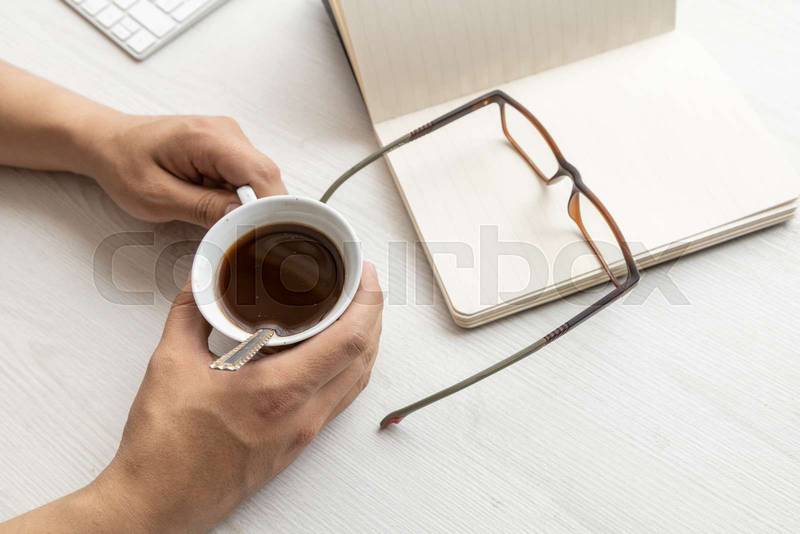 hands holding a cup of coffee, with a notebook, desk of office