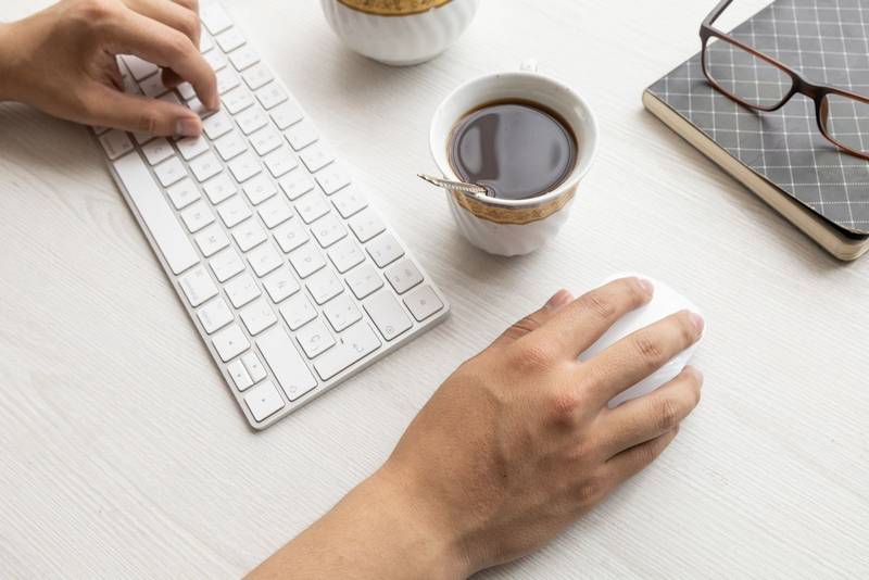 typing on a modern keyboard and using his mouse, around him glasses, cup of coffee, lifestyle at work