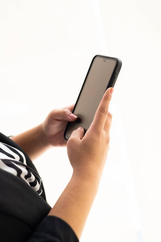 hands typing on a smartphone in an office setting. The image emphasizes communication, technology