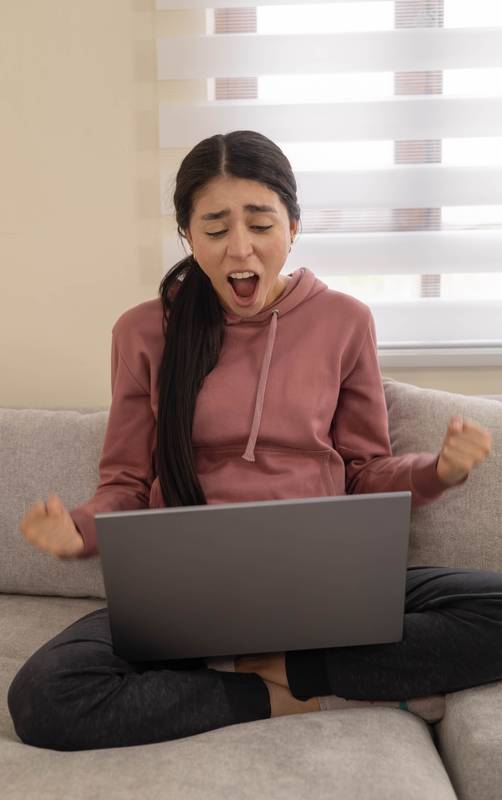 woman yells in frustration while using her laptop on the couch. Concept of digital stress