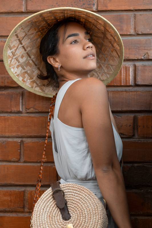 brunette female model smiling standing while playing with her straw hat