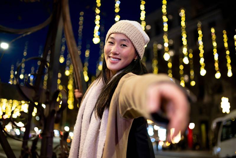 Smiling girl looking at camera enjoying christmas lights in the street. Carefree lady having fun at night in the city during winter.