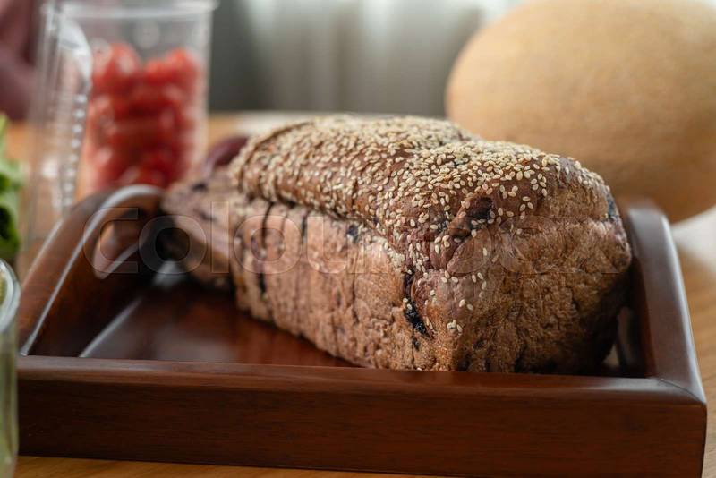healthy breakfast with slices of seeded bread placed on a wooden tray, accompanied by a portion of fresh fruit