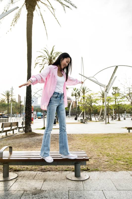 Young happy woman balancing on bench in the street. Carefree and relaxed lady standing on bench park with her arms outstretched in a city.