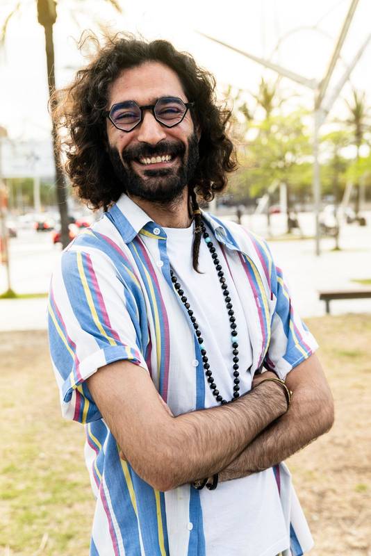 Vertical portrait of happy hipster guy smiling wearing a shirt looking at camera with arms crossed in the street. Side view of a carefree cheerful stylish male wearing glasses 