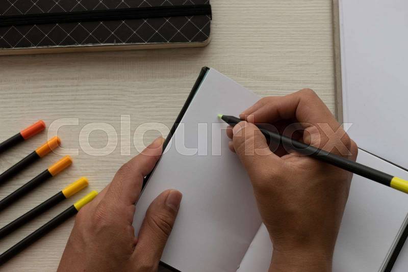 hands writing with a pen on the sheets of a notebook and colored pencils