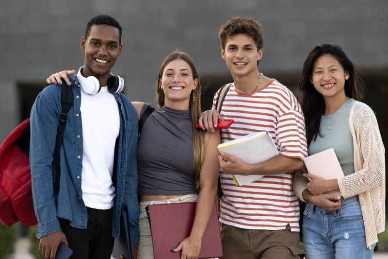 Diverse group of friends standing in the street with folder looking at camera. Multiracial young students smiling staring at camera with confidence and happiness.