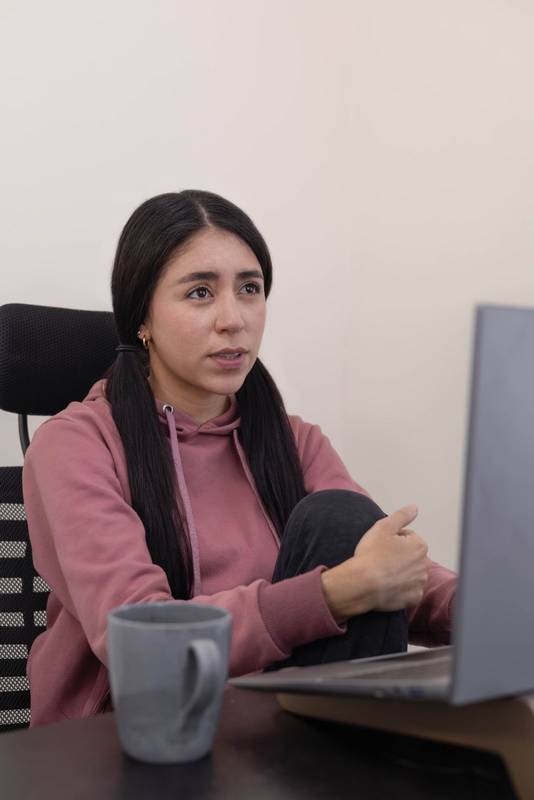 woman sits at her office desk, gazing at her laptop with a bored expression