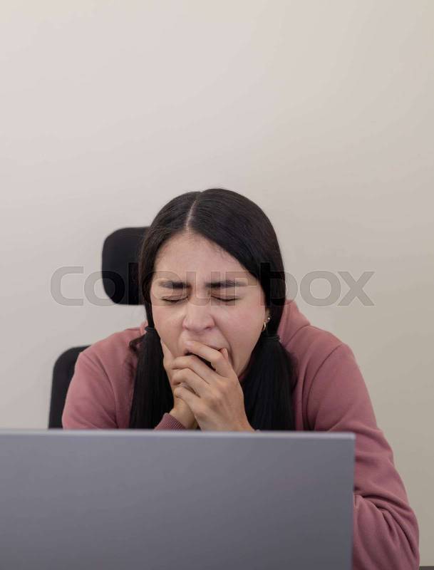 woman sits at her office desk, looking bored and disengaged while staring at her laptop screen
