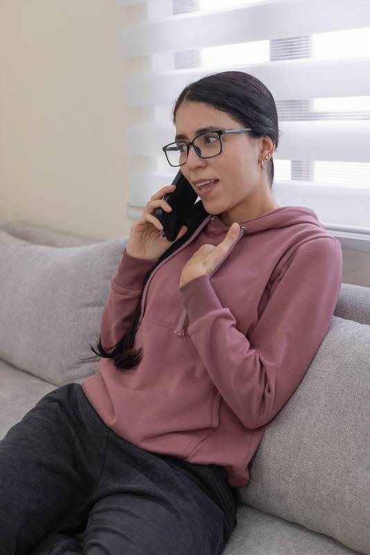 Happy young woman wearing glasses and pink hoodie talk on her smartphone
