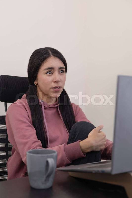 woman sits at her office desk, gazing at her laptop with a bored expression