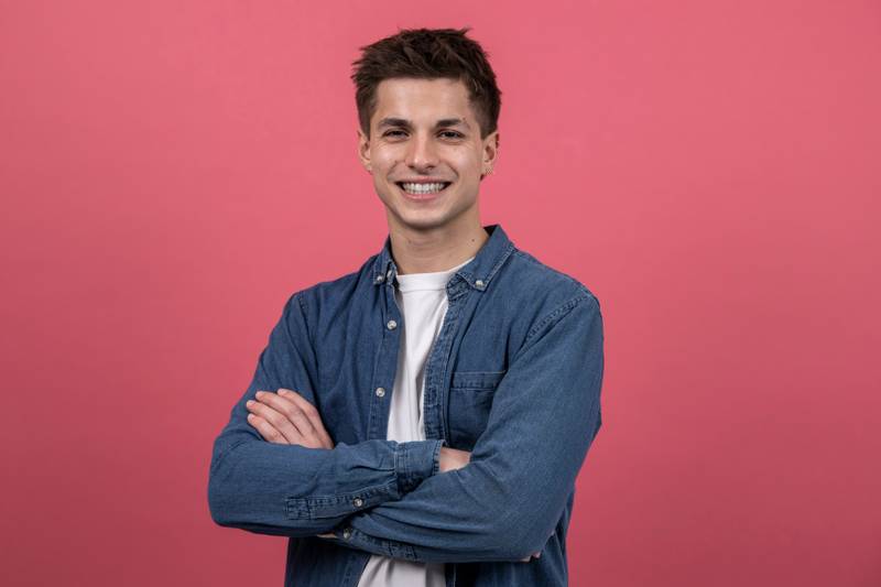 Happy confident laughing guy posing with arms folded. Young relaxed male holding arms crossed looking at camera with confident smile .standing against purple background