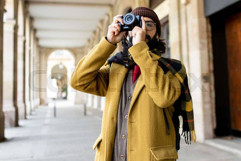 Tourist man taking a photo with his camera in the city. Male photographer having fun on winter vacations on the street