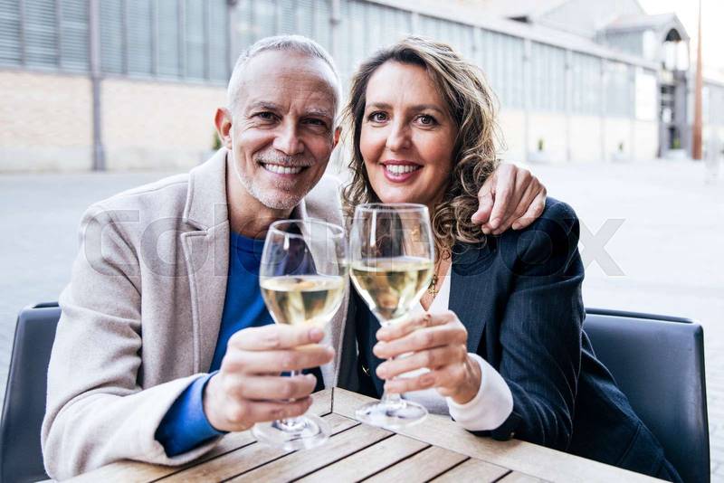 Happy mature couple toasting with wine while sitting in a terrace restaurant. Affectionate middle age woman and man drinking at a terrace looking at camera.