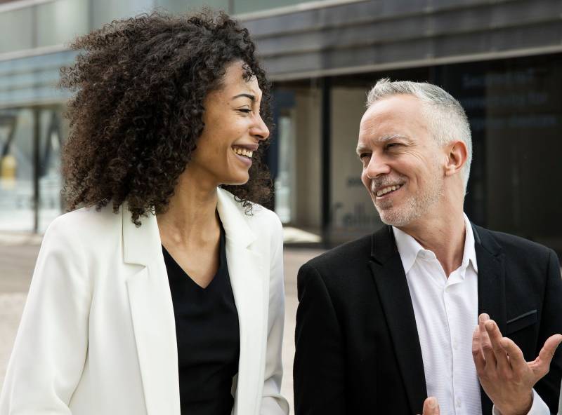 Businesswoman and businessman talking and smiling in the street. Casual meeting between a young executive and a senior ceo having fun outside.