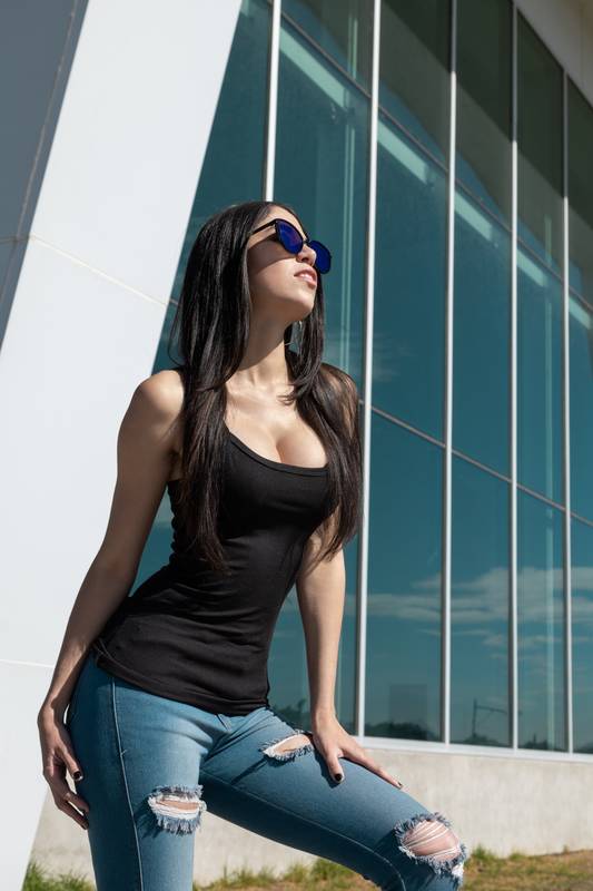 posing standing by a building, wearing casual blouse, fashionable sunglasses and jeans girl