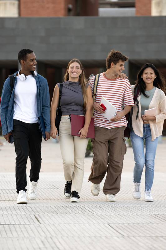 Diverse group of friends walking in the street with folder looking at camera. Multiracial young students smiling staring at camera with confidence and happiness.