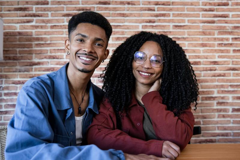 Young adult diverse smiling couple sitting at home looking at camera. Happy relaxed man and woman sitting together in apartment.