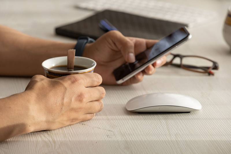 person working at his desk, detail of his hands holding a cell phone with touch screen