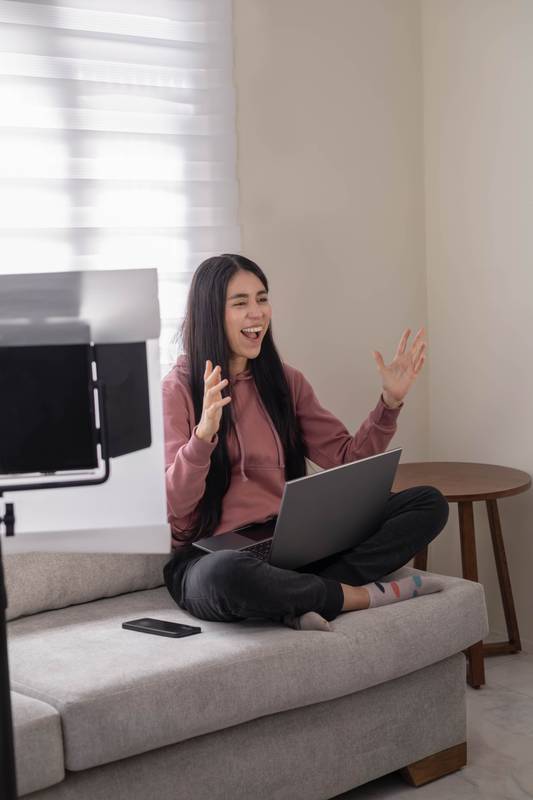 woman sit on the sofa with her laptop, engaged in a cheerful virtual exchange, enjoying a cozy routine while staying connected online.
