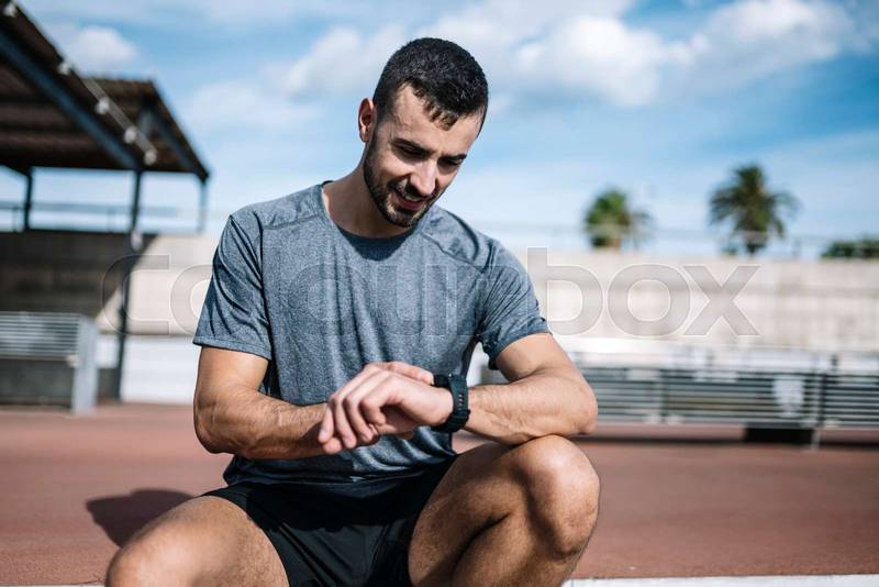 Fitness male looking his watch checking running time after workout. Sports athlete looking smart watch during training outside.