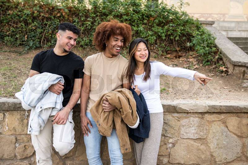 Multiracial young group pointing to the right in a park.Three happy diverse persons smiling and pointing with finger outside.