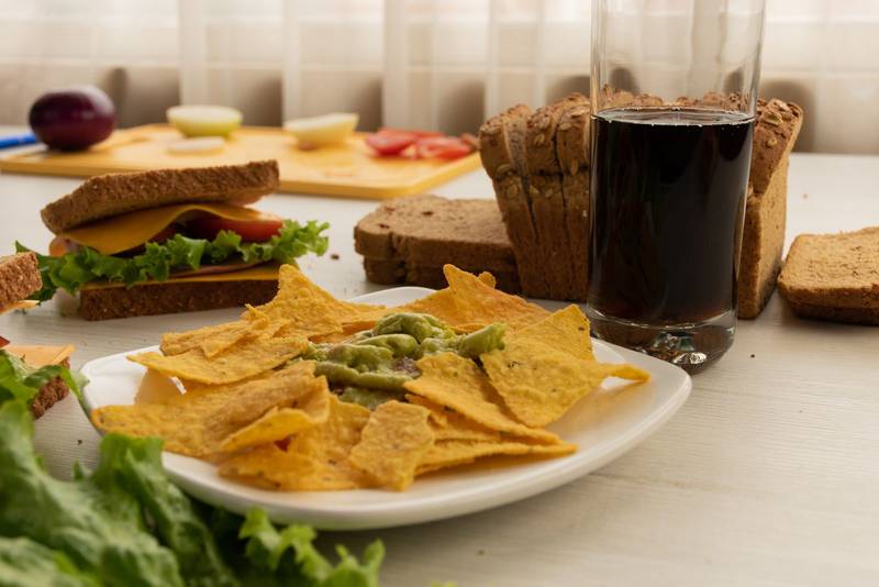 table with a plate of crunchy nachos accompanied by guacamoles, sandwich
