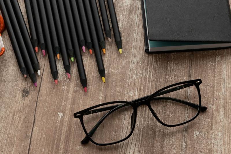 notebook with colored pencils and glasses on a wooden textured table, instruments in workspace