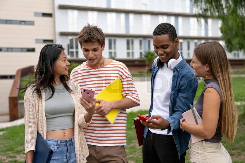 Diverse group of friends checking their phones and holding folders.Happy multiracial friends using smartphones and carrying files in a campus.