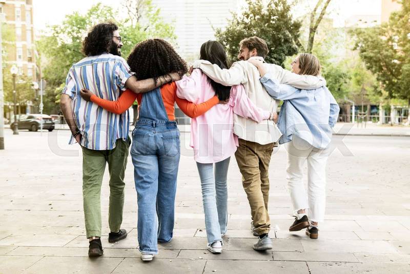 Back view of diverse people hugging each other while walking in the street. Rear view of a group of friends embracing and enjoying the city together.