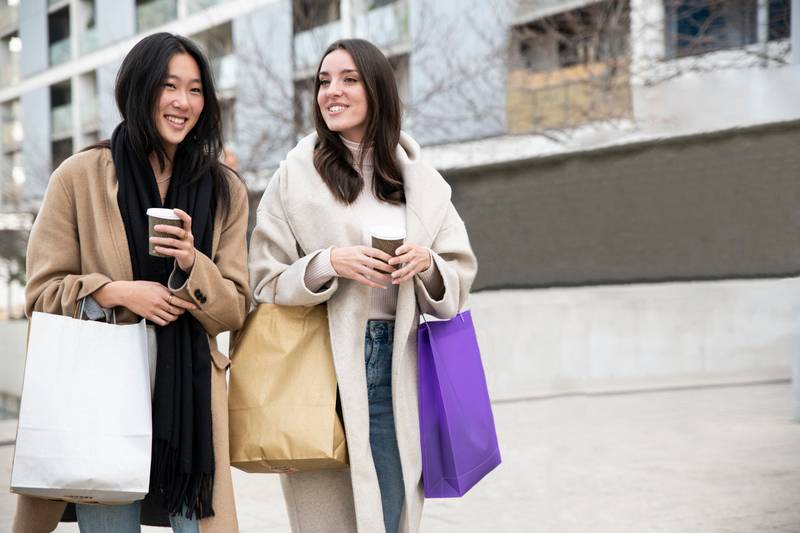 two happy young beautiful women walking on the street holding shopping bags ang cup of coffee. cheerful friends enjoying together in the mall.
