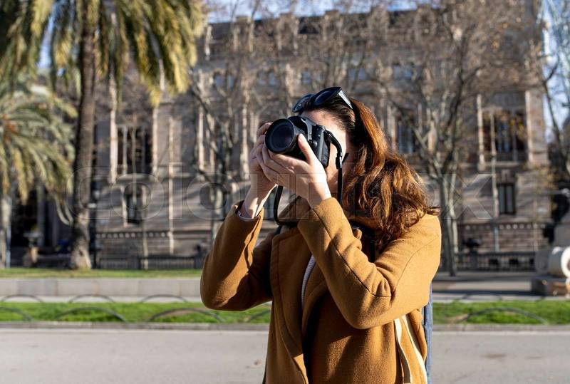 smiling woman traveler holding a camera at the city in holidays - relaxation, tourism concept