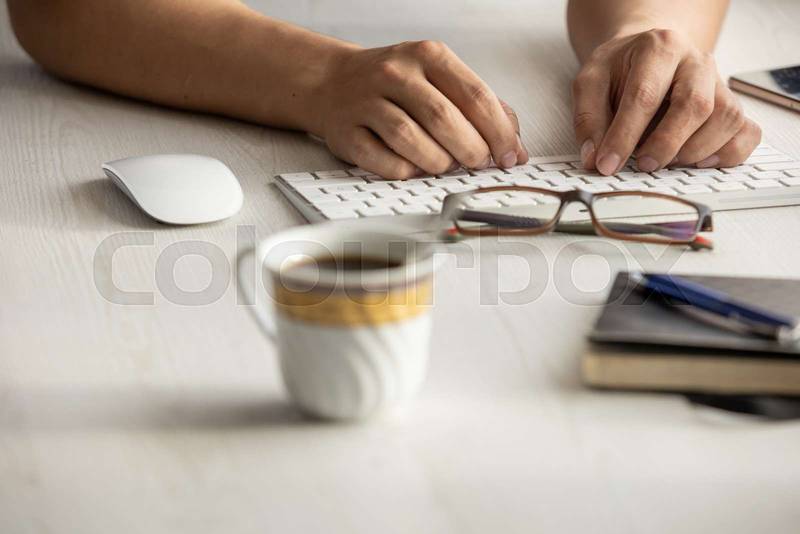 hands of a person holding a cup with hot coffee on a wooden desk