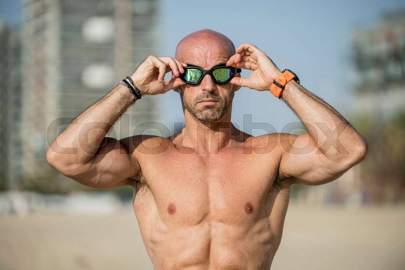 Confident man putting on swim glasses to go in the ocean. Serious male swimmer preparing to go for a swim in the beach.
