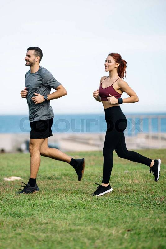 Happy athletic male and female in sportswear training workout outside. Young adult couple running together in a park while jogging. 