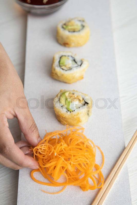 decorating a plate with carrots and sushi roll with rice, food detail, lifestyle, restaurant