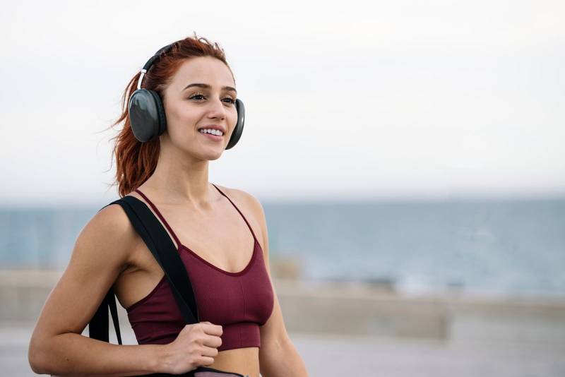 Fit sport woman relaxed listening music going to the gym. Young female athlete wearing headphone smiling on her way to training and workout.