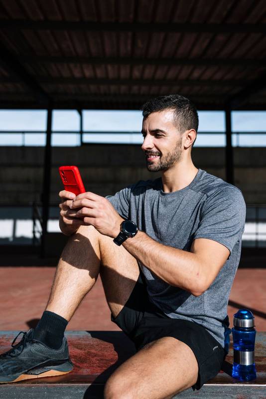 Fit man using smartphone relax resting from exercise in a bench outside. Active sports athlete texting with phone during training.