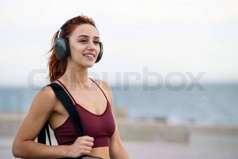 Fit sport woman relaxed listening music going to the gym. Young female athlete wearing headphone smiling on her way to training and workout.
