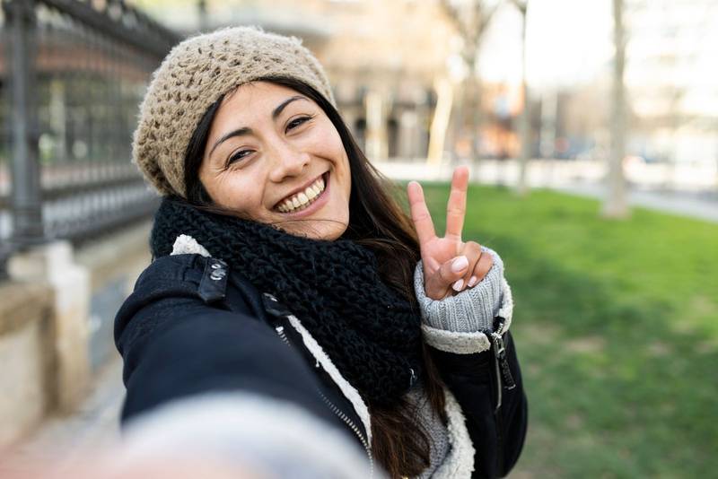 happy woman making a selfie showing two finger in the city. Cheerful portrait of a young female tourist. Holidays, people concept