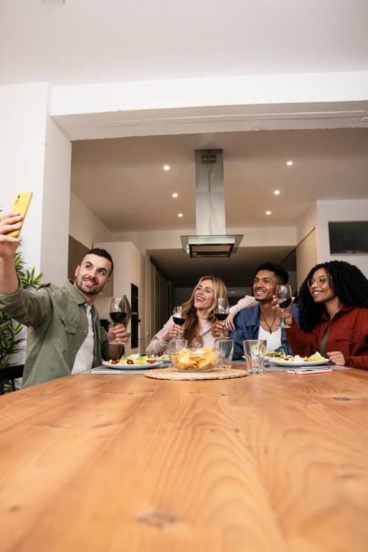 Smiling people taking selfie while eating on a modern apartment. Cheerful Diverse group of happy friends having video call diner at home. 