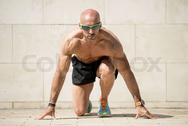 Strong male athlete ready to start running. Fit runnner man preparing for a run in the street.