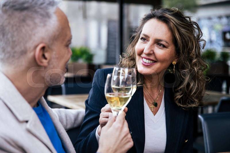 Smiling couple toasting with wine while sitting in a restaurant. Happy middle age woman and man drinking at a terrace looking each other.