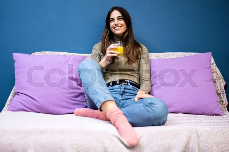 Happy young woman sitting on sofa at home and looking at camera. Portrait of comfortable caucasian woman similing and relaxing on armchair