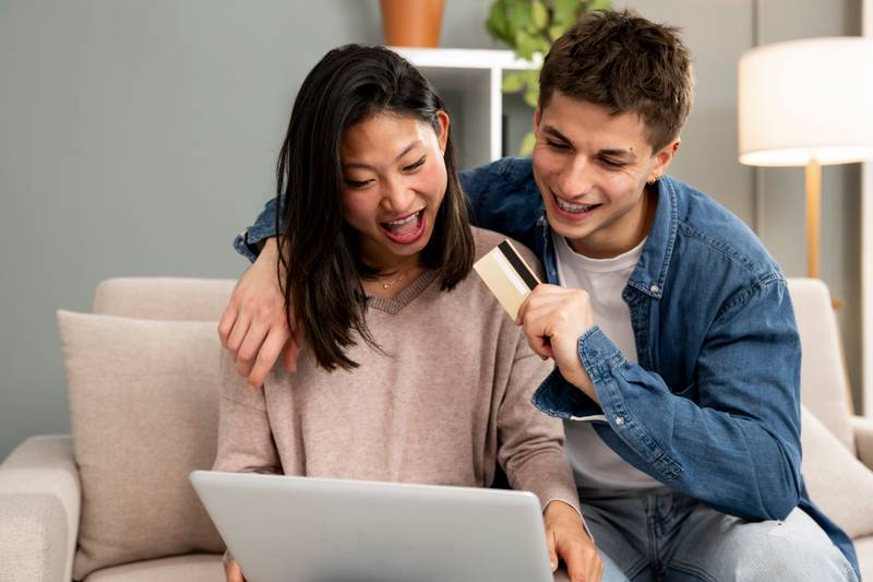Young carefree diverse couple shopping online with laptop in a sofa. Happy man and woman happy for paying with credit card using a computer at home.